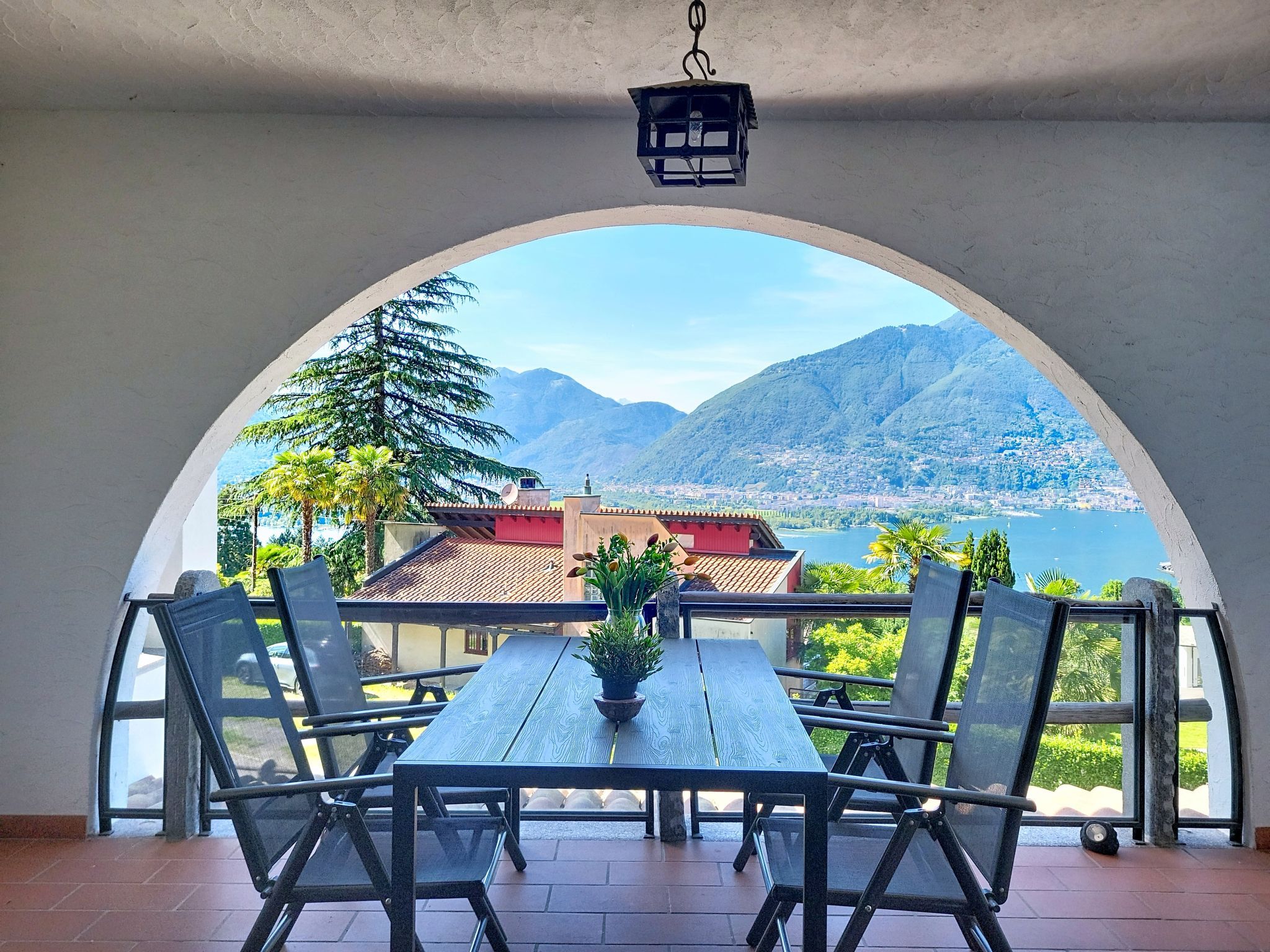 Un espace extérieur aménagé avec une table et des chaises, offrant une vue sur un paysage montagneux et une étendue d’eau.