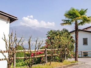 A coastal view with a mountain in the background, a palm tree, and a wooden fence. - Residenza Miralago Apt.D31 by Interhome (Piazzogna)