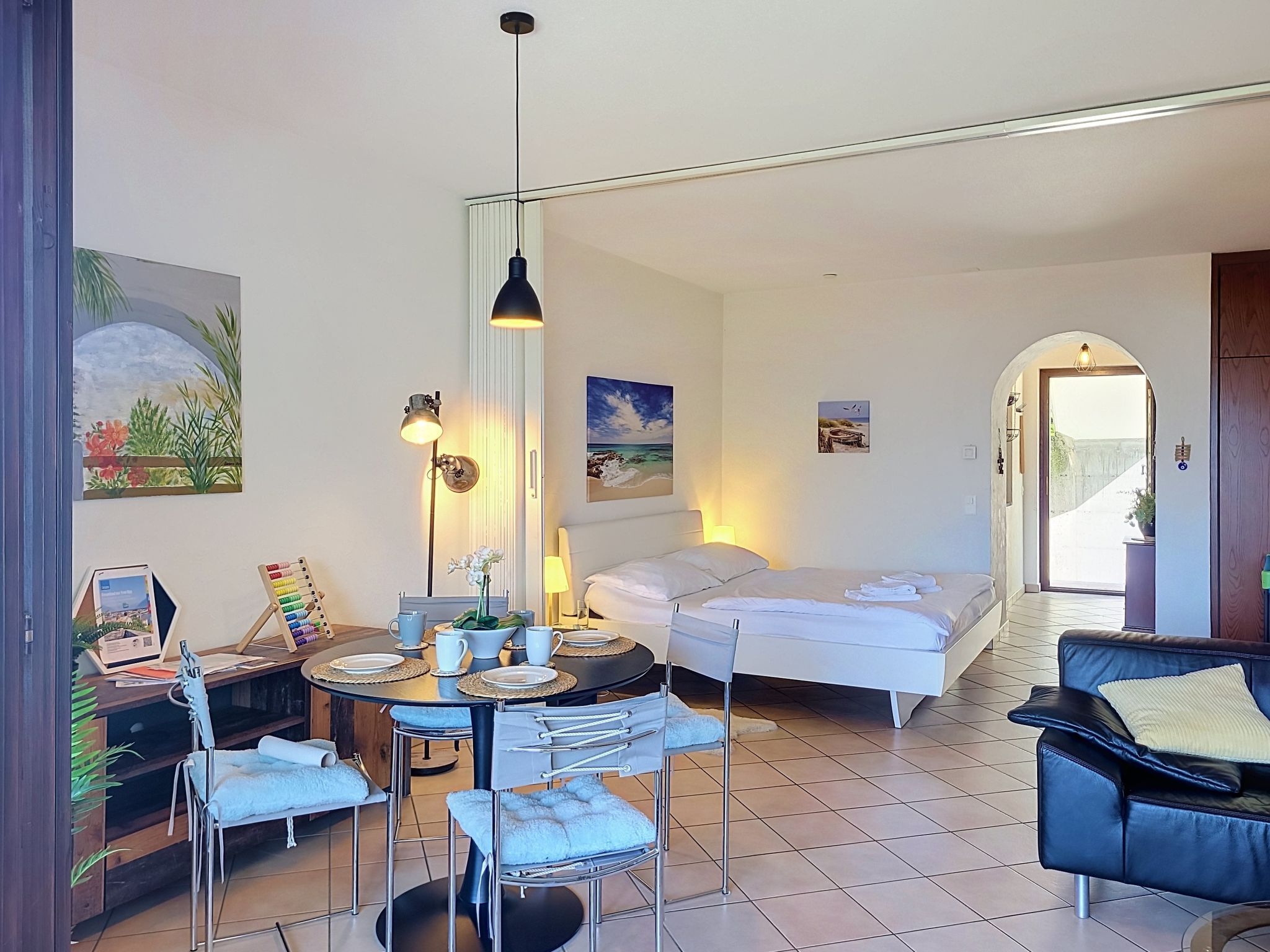 A hotel room with a bed, a dining area with a table and chairs, and artwork on the walls.