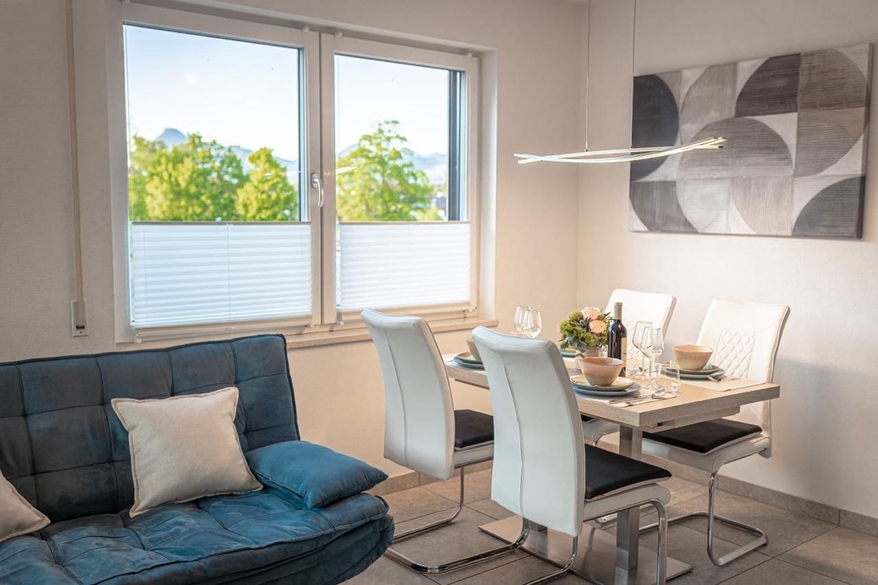 Un espace de repas moderne avec une table dressée pour deux personnes, un canapé et une vue par la fenêtre.