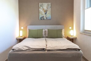 Una cama con cabecera, dos mesitas de noche con lámparas, y un cuadro en la pared.