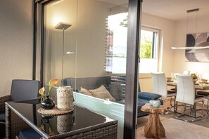 Una sala de estar moderna con un separador de vidrio, un comedor con mesa y sillas, y vista al exterior.