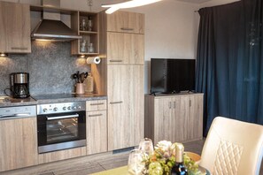 A modern kitchen with wooden cabinets, a built-in oven, a coffee maker, and a flat-screen TV. - SOLIM: Kitchen, balcony & garden, 45 square meters, max. 4 people. (Kiefersfelden)