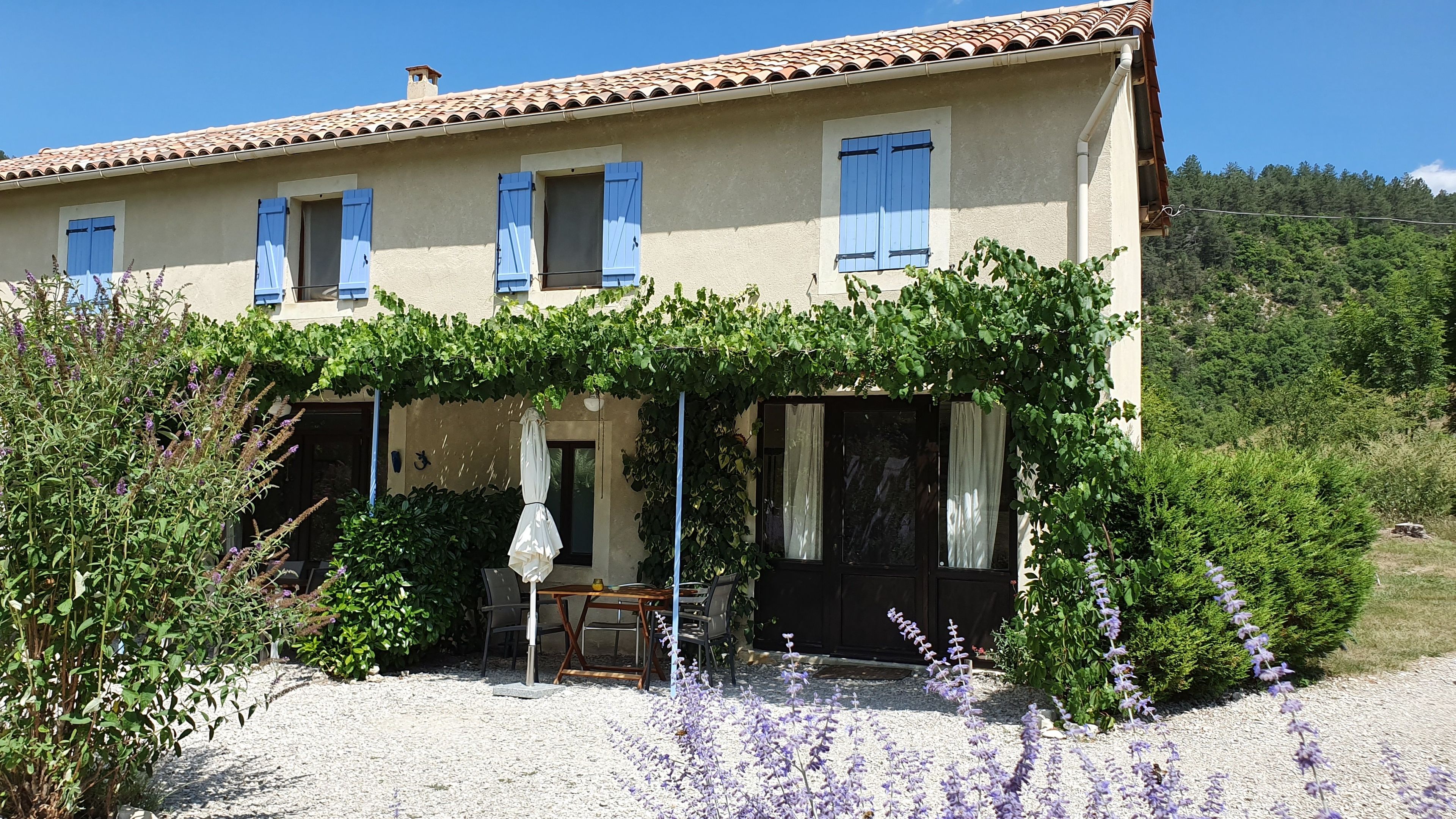 A two-story building with a tiled roof, blue shutters, and a covered porch with a table and chairs.