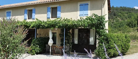 A two-story building with a tiled roof, blue shutters, and a covered porch with a table and chairs.
