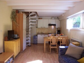 A compact kitchen with white cabinets, a dining area with wooden chairs, a small table, and a window with a view of greenery. - Gîte Soleil with pool, adults only (18+) (Beaumont-en-Diois)