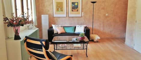Una sala de estar con un sofá, una butaca, una mesa de centro y dos cuadros enmarcados en la pared.