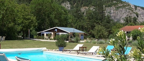 A swimming pool with lounge chairs, a small building, and a mountainous backdrop.