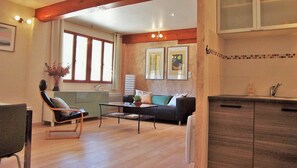A living room with a sofa, a coffee table, a chair, and a kitchen area with cabinets. - Holiday Home 'Papillon' with Pool, Minimum Age 18 (Beaumont-en-Diois)