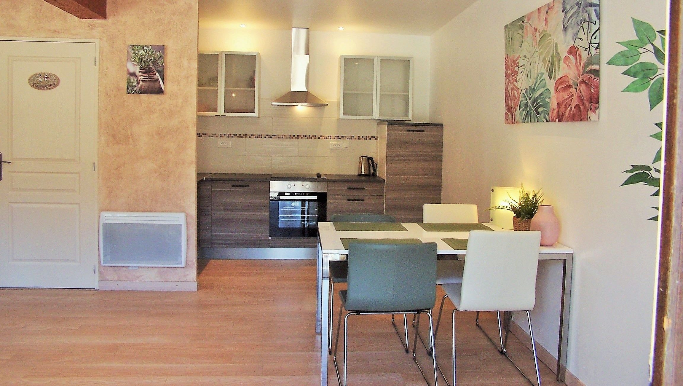Una cuina moderna amb forn integrat, una zona de menjador amb taula i cadires, i una porta que dona a un altre espai.