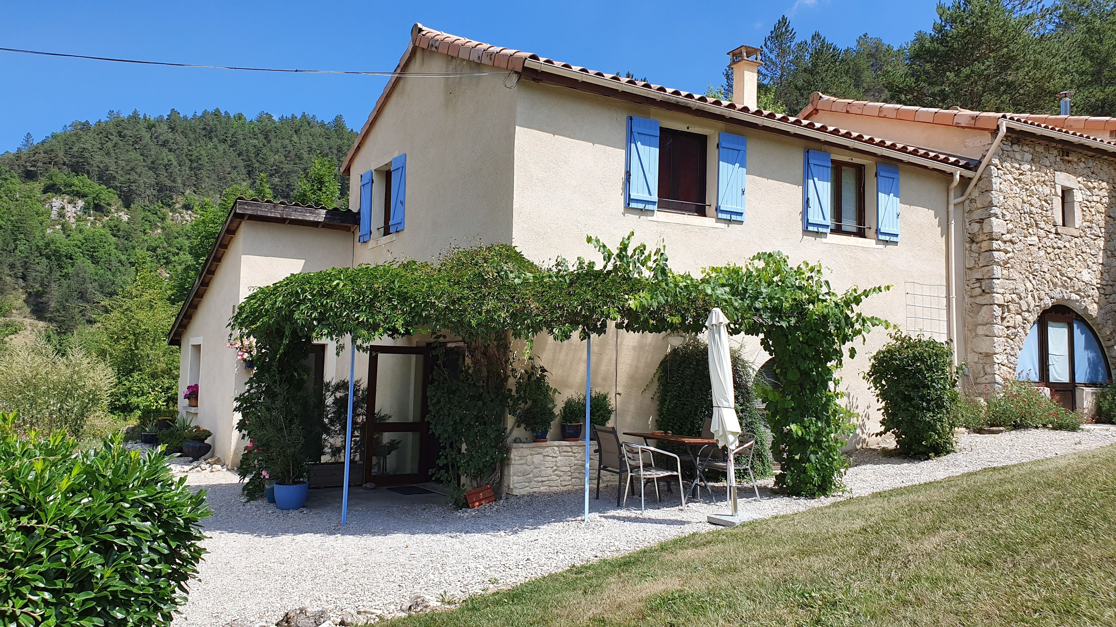 A two-story house with a stone facade, blue shutters, and a covered patio area with outdoor furniture.
