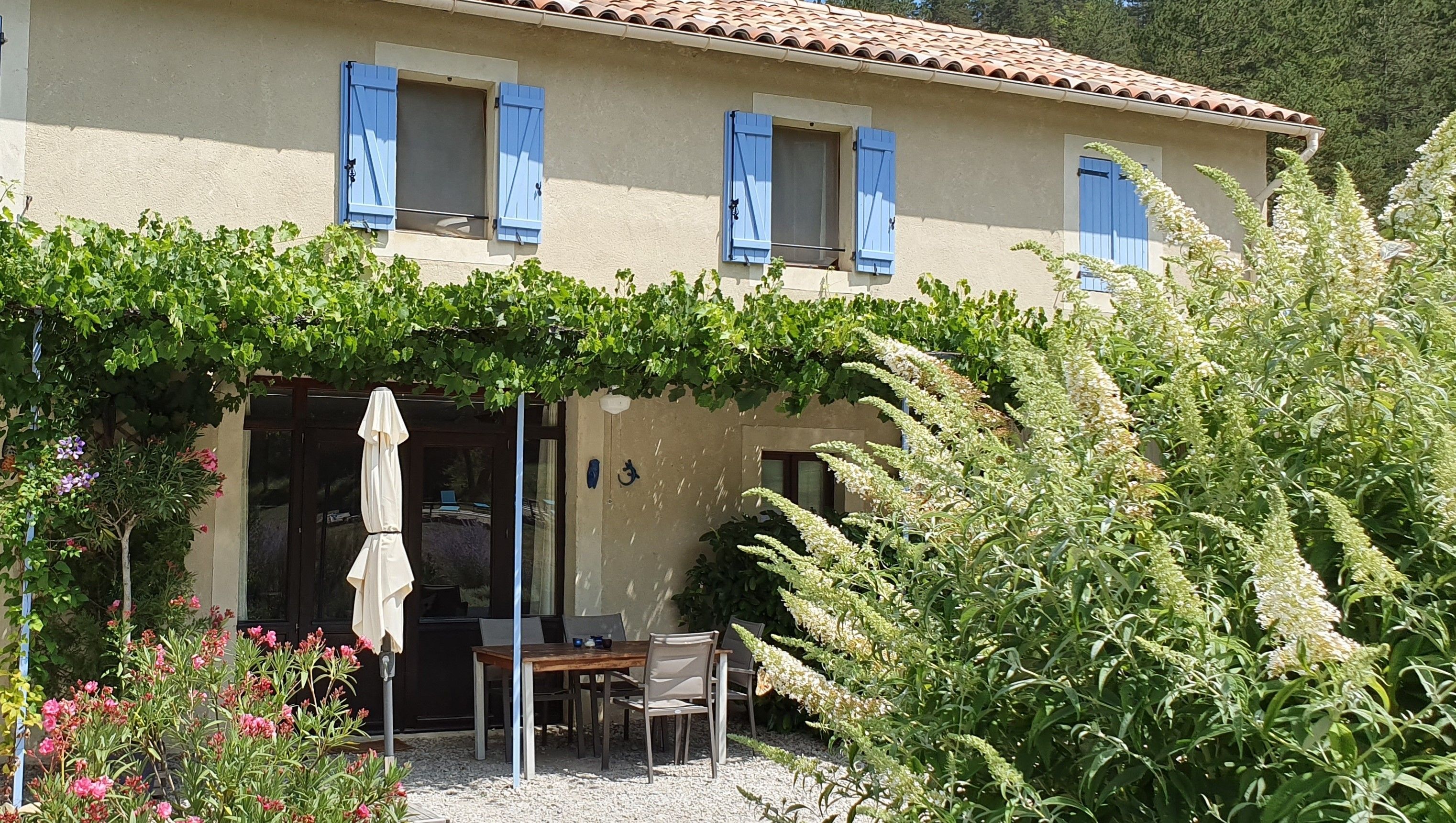 A building with a covered patio area, a table and chairs, and a variety of plants and flowers.