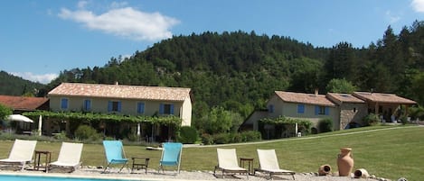 A pool area with lounge chairs and a view of a hillside with buildings.