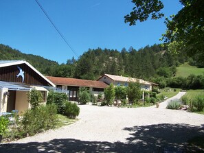 Ein ländliches Anwesen mit einem Schotterweg, der zu einem Haus mit Ziegeldach führt, umgeben von viel Grün und Hügeln.
