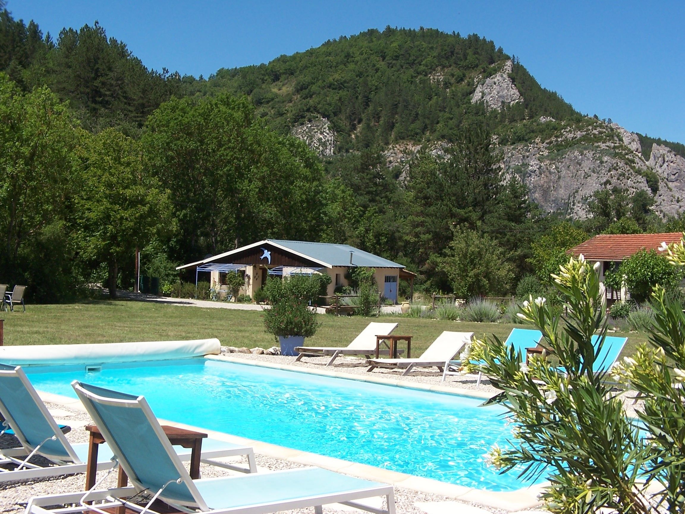 Una piscina amb gandules, un edifici petit i un paisatge de muntanyes al fons.