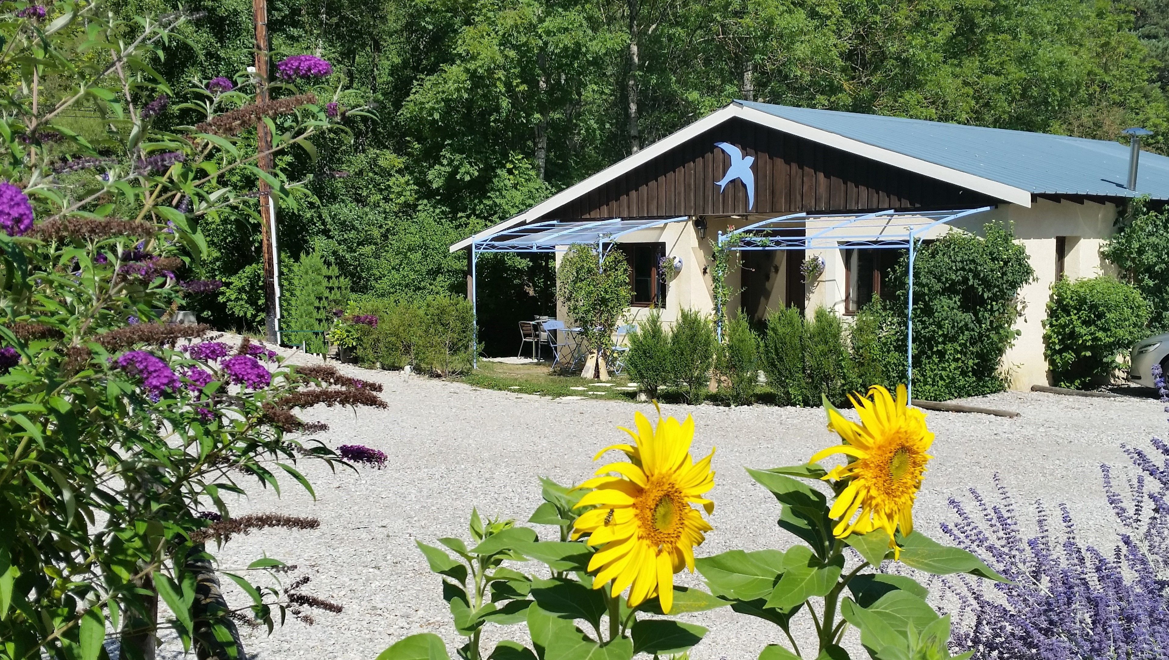 A building with a covered outdoor area, surrounded by greenery and flowers.