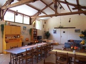 Eine geräumige Küche mit Holzbalken, ein Essbereich mit einem langen Tisch und Stühlen sowie ein gemütlicher Wohnbereich mit einer Couch und einem Fernseher.