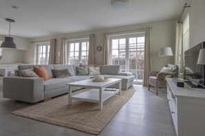 A modern living room with a sofa, coffee table, and a view of the outdoors through large windows. - Apartment in Cadzand-Bad with swimming pool (Cadzand-Bad)