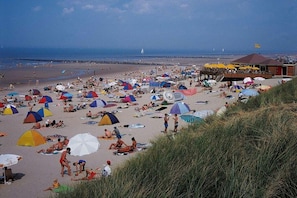 Ein Strand mit Zelten und Sonnenschirmen, einem Rettungsturm und einem klaren Himmel.