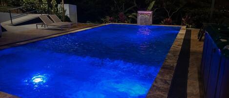 Une piscine dotée d’un élément décoratif aquatique illuminé de lumière bleue et d’une petite cascade.