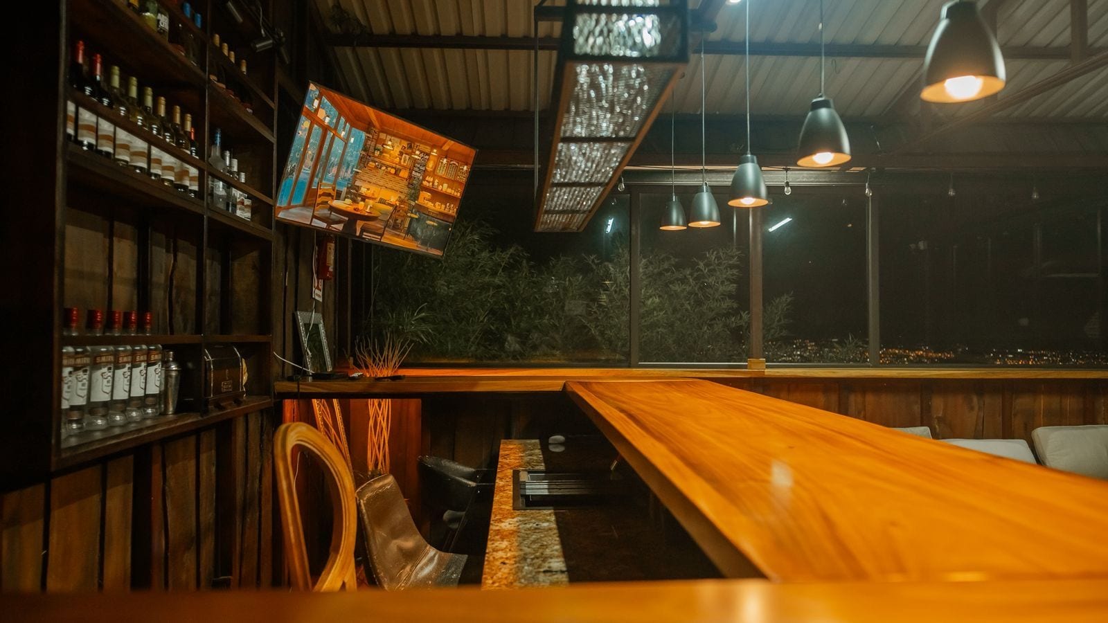 A bar area with wooden shelves stocked with bottles, a long wooden counter, and hanging pendant lights.