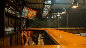 A bar area with wooden shelves stocked with bottles, a long wooden counter, and hanging pendant lights.