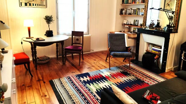 A cozy living room with a fireplace, a bookshelf, a dining area with a table and chairs, and a colorful rug. - Charming 1‑Bedroom Apartment 500 m from Paris – RER B 2 min – Cité Universitaire (Gentilly)
