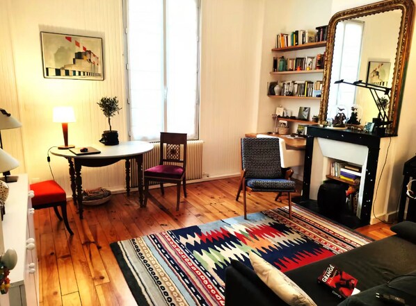 Ein gemütliches Wohnzimmer mit Kamin, Bücherregal, Essbereich mit Tisch und Stühlen sowie einem farbenfrohen Teppich.