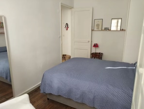 Ein Schlafzimmer mit einem Bett, einer Tür, einem kleinen Tisch mit einer Lampe und einem Regal mit Bildern.