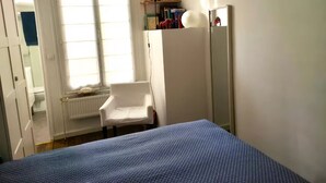 A bedroom with a bed, a chair, a radiator, a window, and a mirror. - Charming 1‑Bedroom Apartment 500 m from Paris – RER B 2 min – Cité Universitaire (Gentilly)