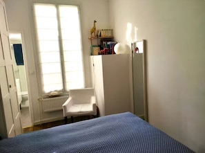 Ein Schlafzimmer mit Bett, Stuhl, Heizkörper, Fenster und Spiegel.