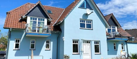 Een huis met twee verdiepingen, een balkon, een schotelantenne en een kleine tuin.