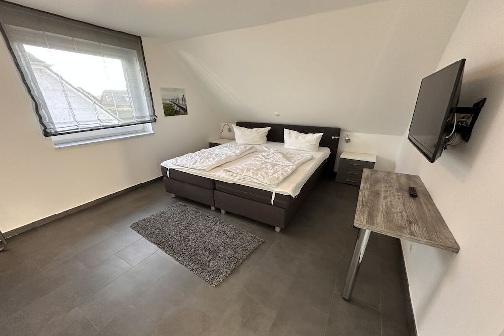 Quarto com cama, escrivaninha, televisão, janela e tapete.
