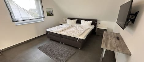 Quarto com cama, escrivaninha, televisão, janela e tapete.