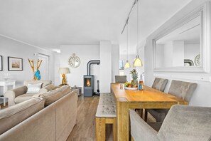A modern living room with a sofa, a dining table with chairs, a fireplace, and a large mirror. - SchleiZeit: Vacation Home in the Olpenitz Baltic Sea Resort with Sauna, Hot Tub, and Ocean View (Olpenitz)