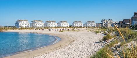A beachside hotel with multiple white buildings, sandy beach, and clear blue sky.