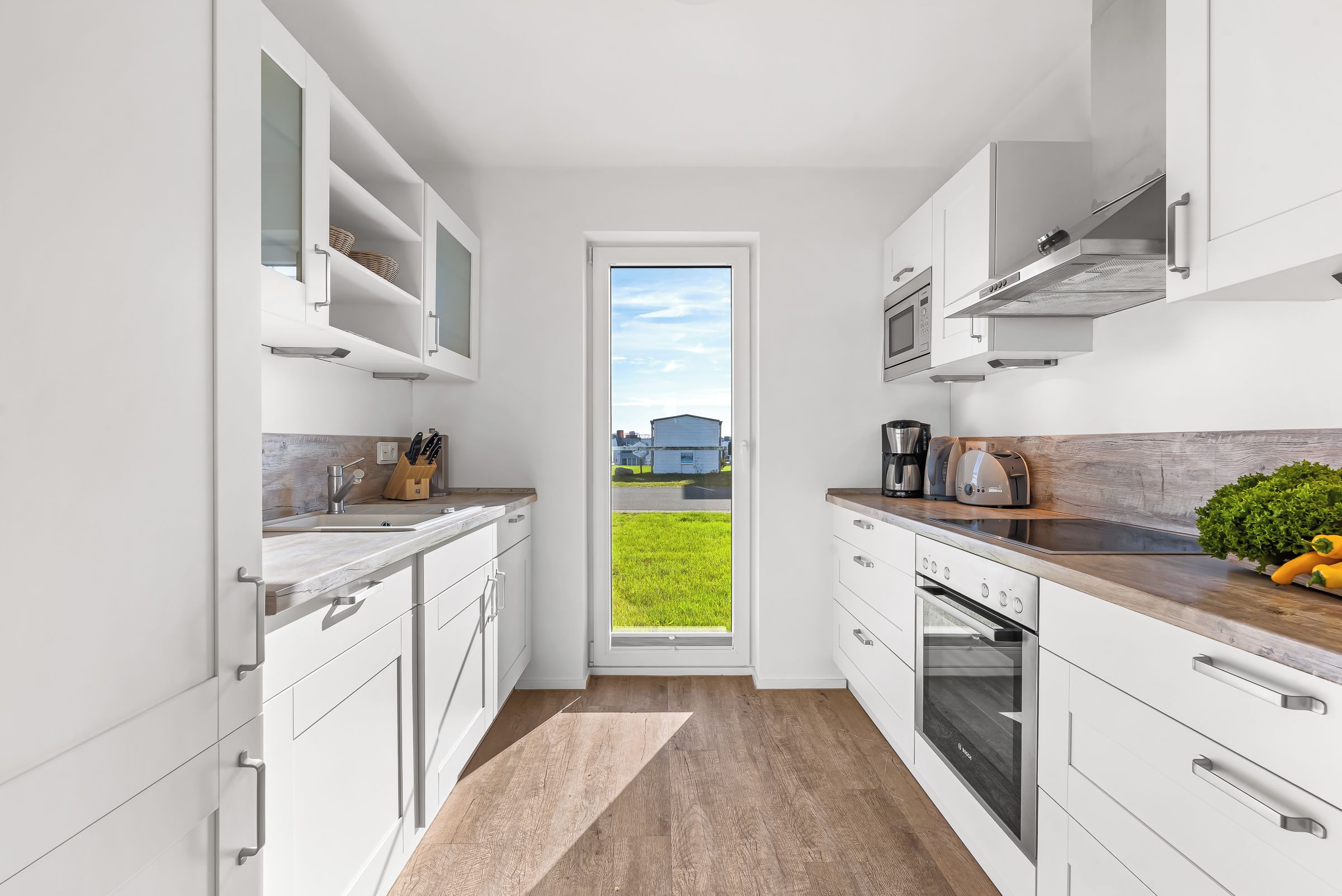 A modern kitchen with white cabinetry, a built-in oven, and a window overlooking a grassy area.