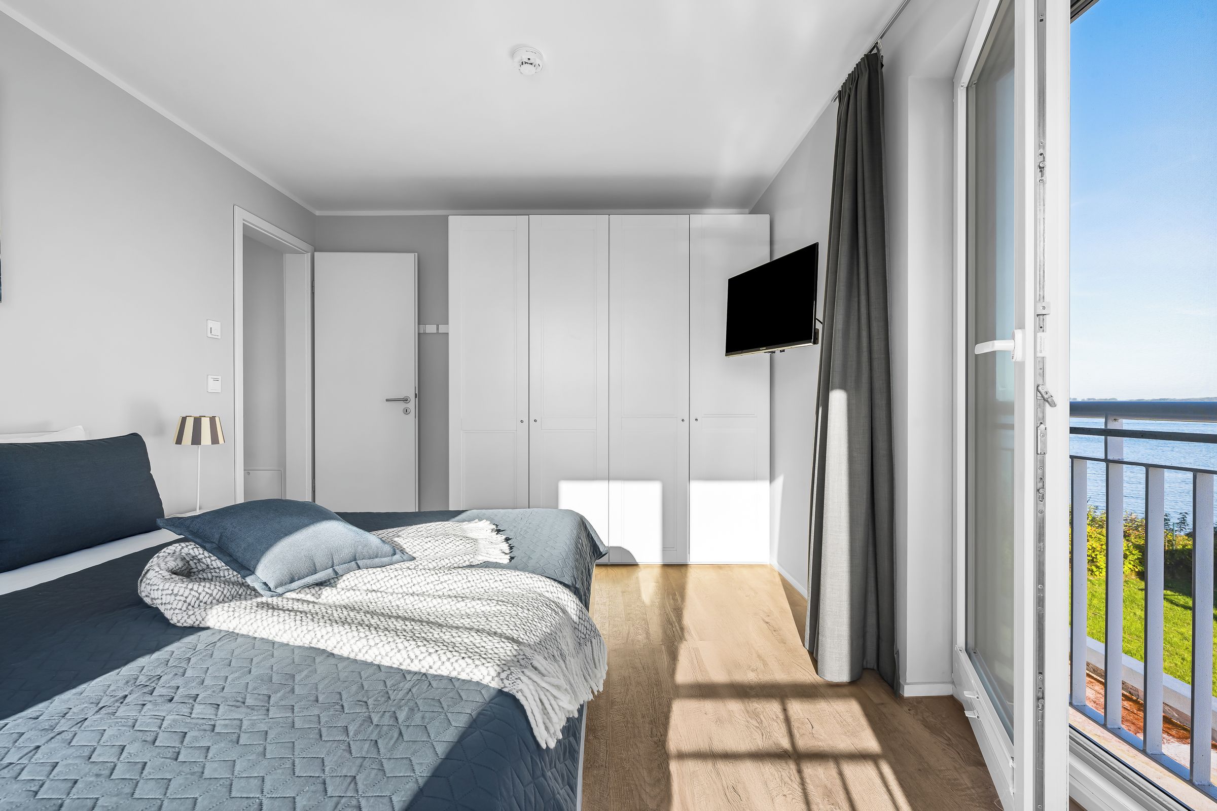 A bedroom with a bed, a TV, and a balcony with a view.