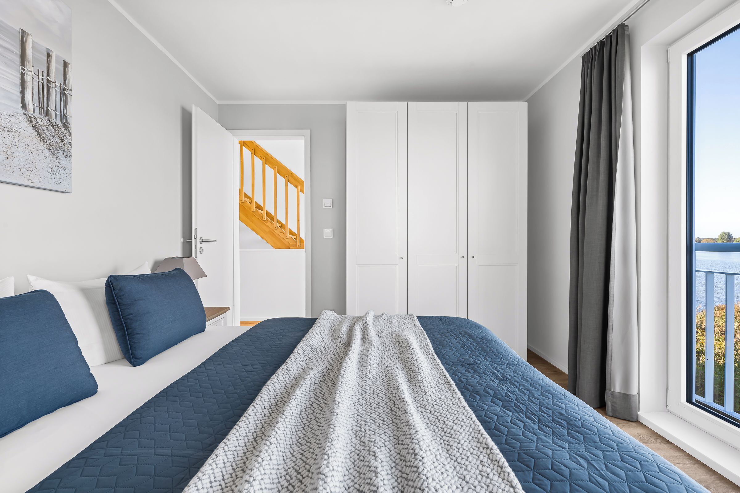 A bedroom with a bed, a view of the outside, and a staircase leading to another room.