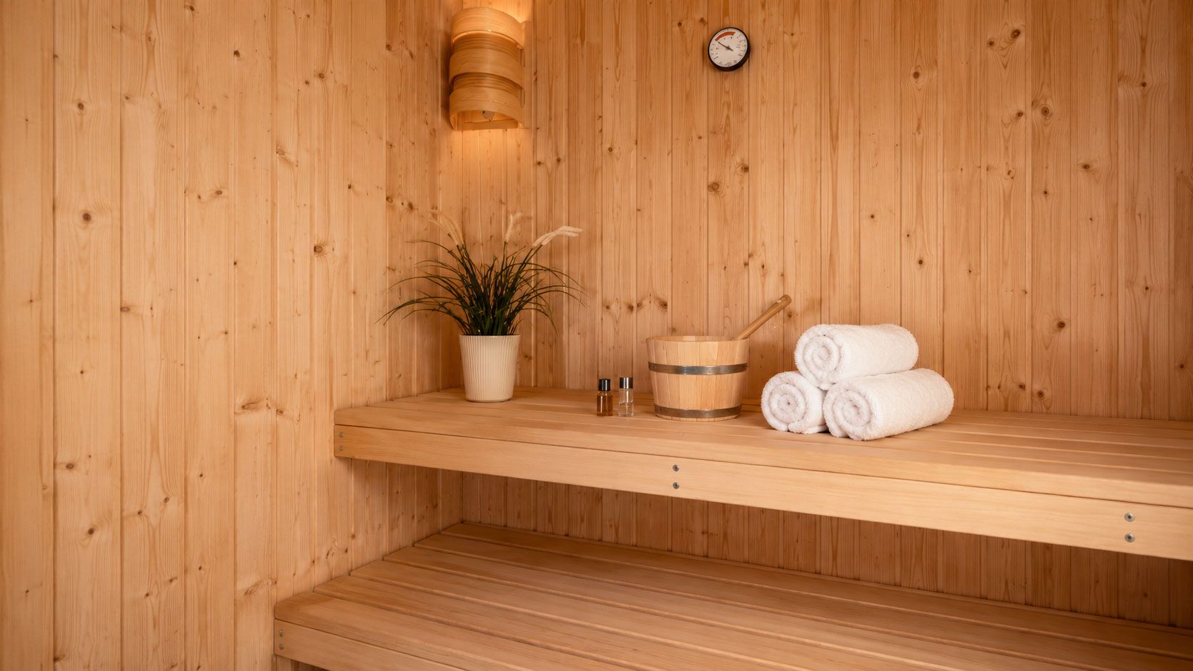 Een houten sauna met een plank waarop een plant, een emmer en opgerolde handdoeken staan.