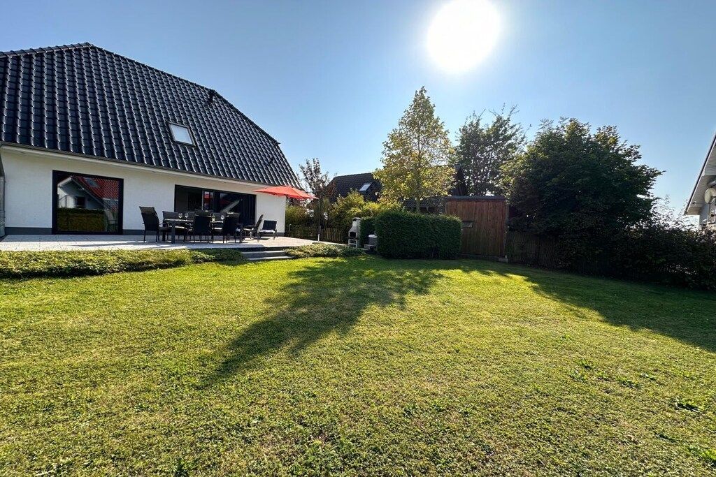 A residential property with a well-maintained lawn, a patio area with outdoor furniture, and a house with a tiled roof.