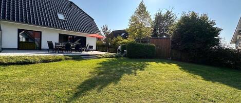 Una propiedad residencial con un césped cuidado, un patio con mobiliario exterior y una casa con tejado de tejas.