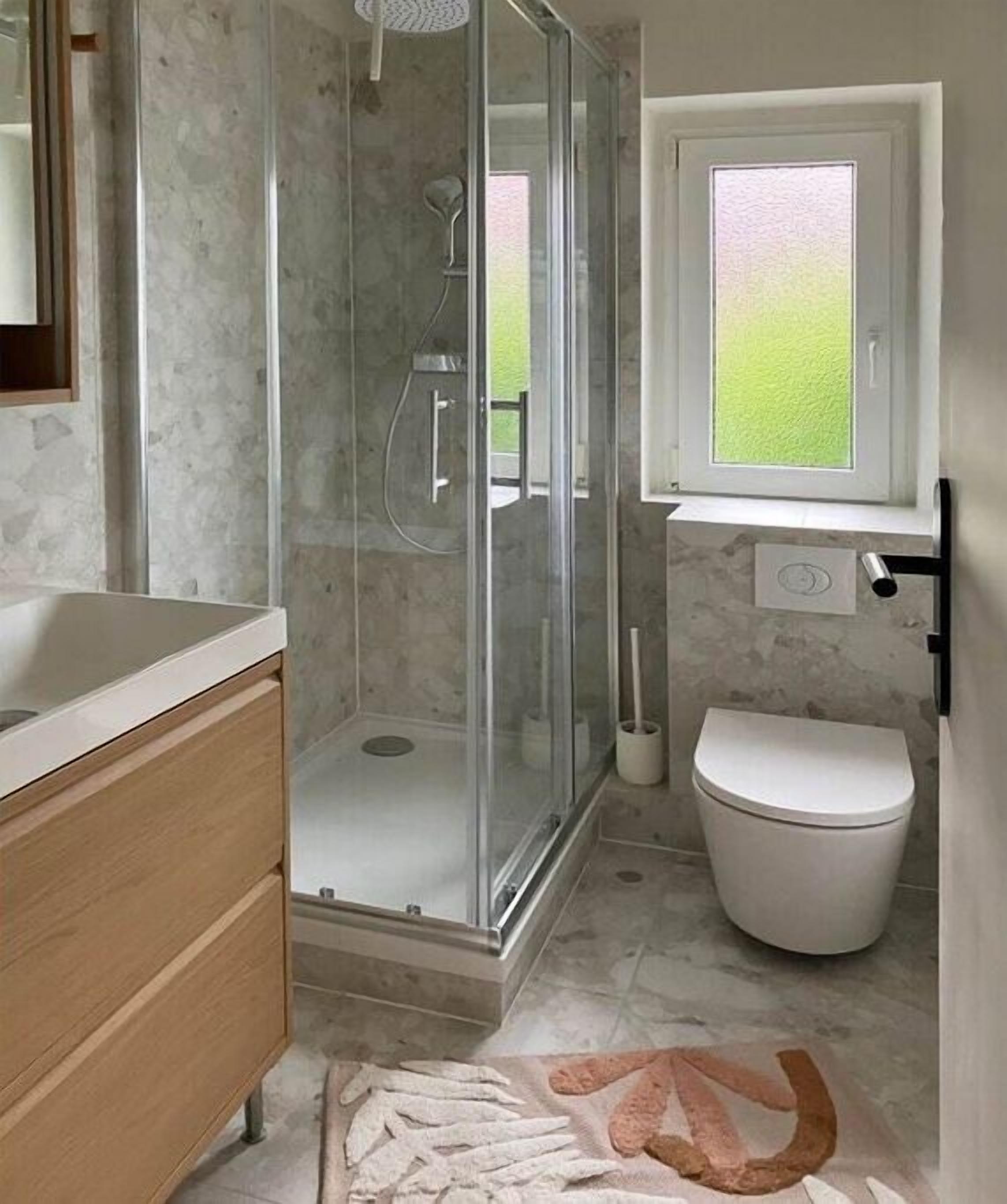 A bathroom with a glass-enclosed shower, a toilet, and a sink with a wooden cabinet.