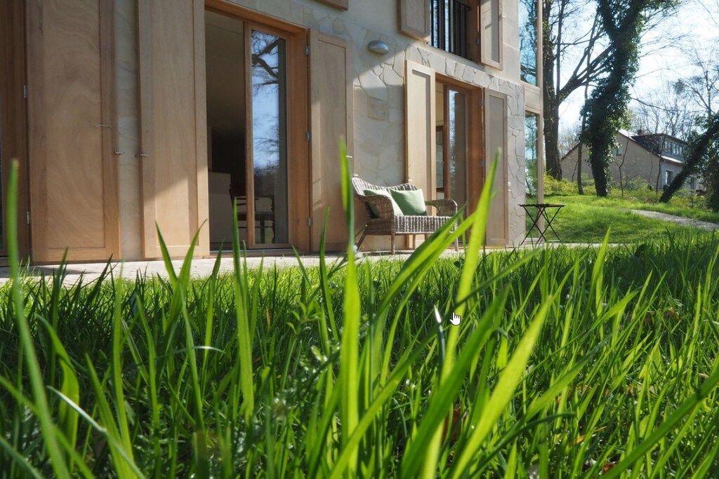 A modern house with a glass door entrance, a small patio with a chair, and a grassy lawn.