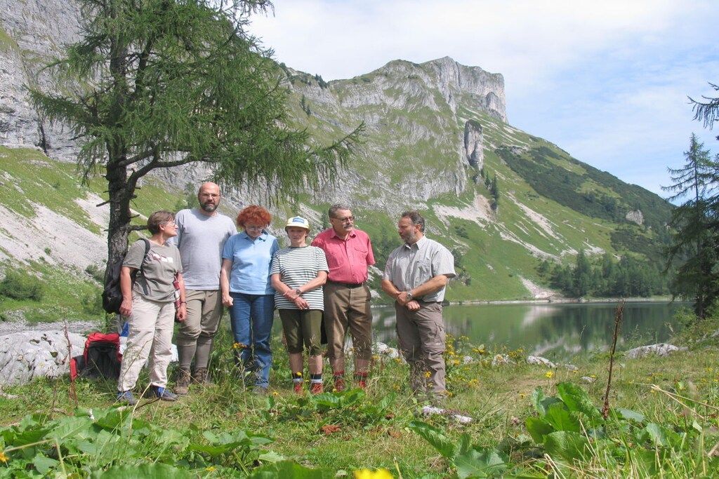 Een groep mensen staat op een grasveld, met een berg en een meer op de achtergrond.