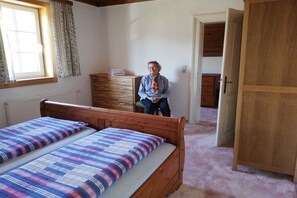A bedroom with two beds, a wooden dresser, a window with curtains, and a door leading to another room. - Holiday home with 1 bedroom (GRUNDLSEE)