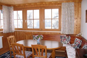 A wooden-paneled room with a round table, chairs, and a bench with floral cushions. - Holiday home with 1 bedroom (GRUNDLSEE)