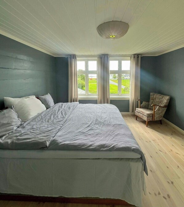 A bedroom with a large bed, a chair, and a window with curtains.