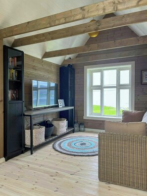 Una sala de estar acogedora con techo de madera, un ventanal con vistas, un televisor y una estantería.