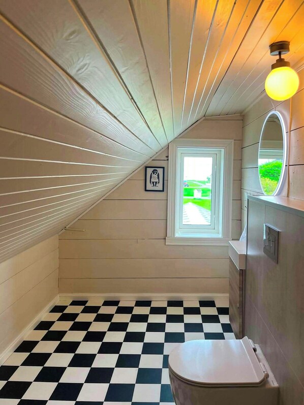 A bathroom with a checkered floor, a toilet, a window with a view, and a mirror with a light fixture.